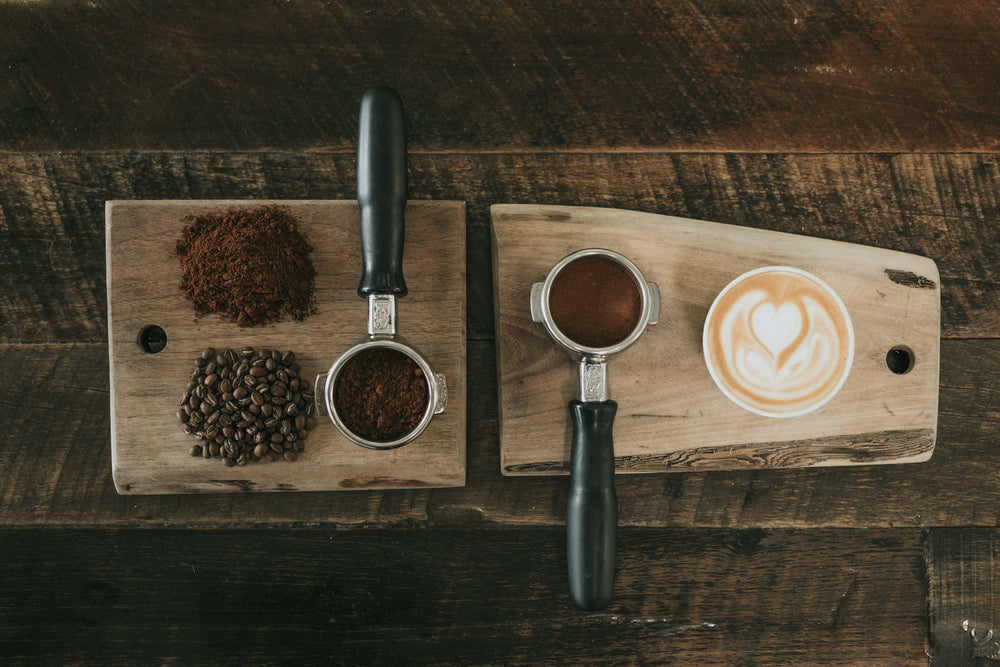 Kavna zrna, sveže mleta kava v portafiltru in pripravljen cappuccino na leseni mizi.