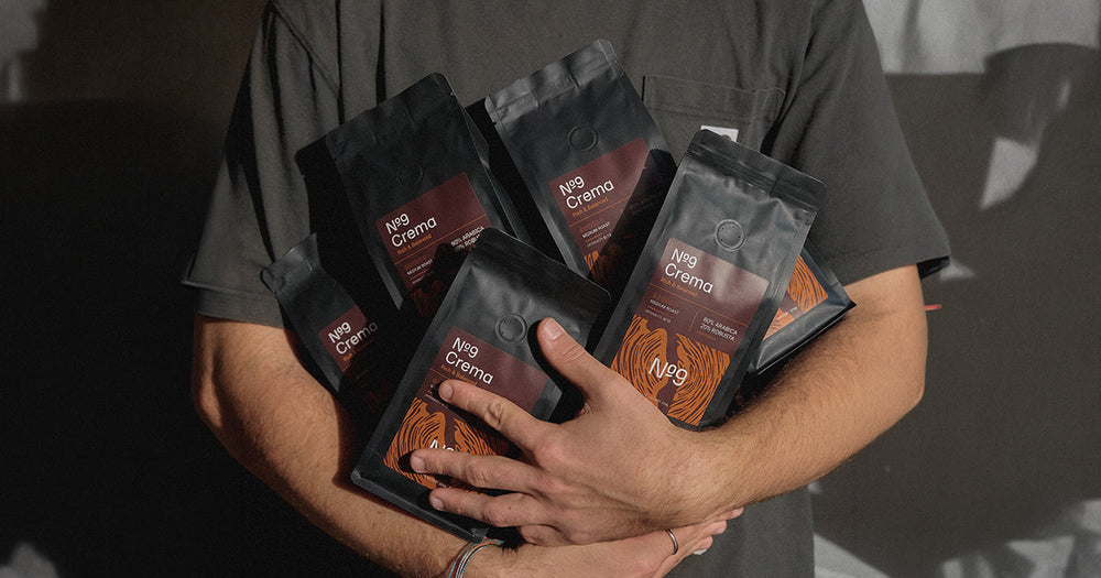 Oseba drži več pakiranj kave v zrnju №9 Caffè Aroma, Crema in Forte.