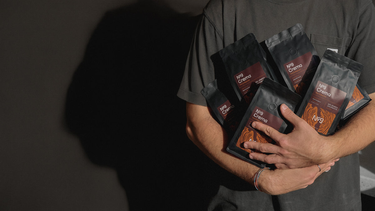 Oseba v naročju drži več 250 g vrečk kave v zrnju No9 Caffè Crema in Aroma